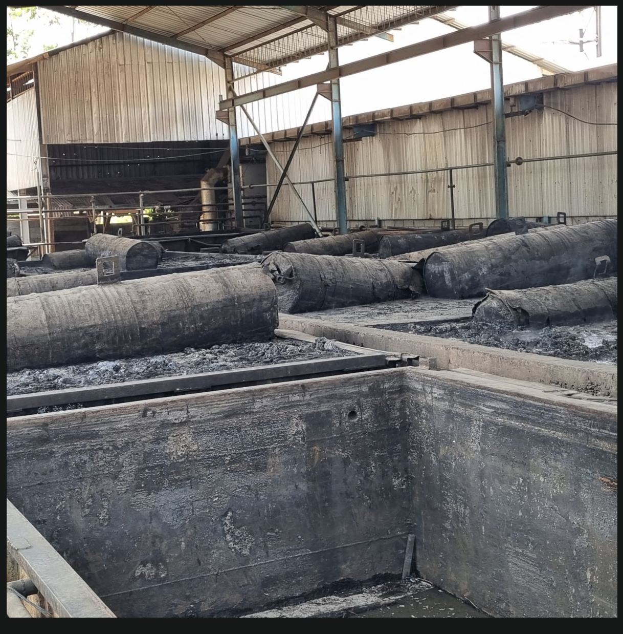 Logs conditioning in vats under a factory shed